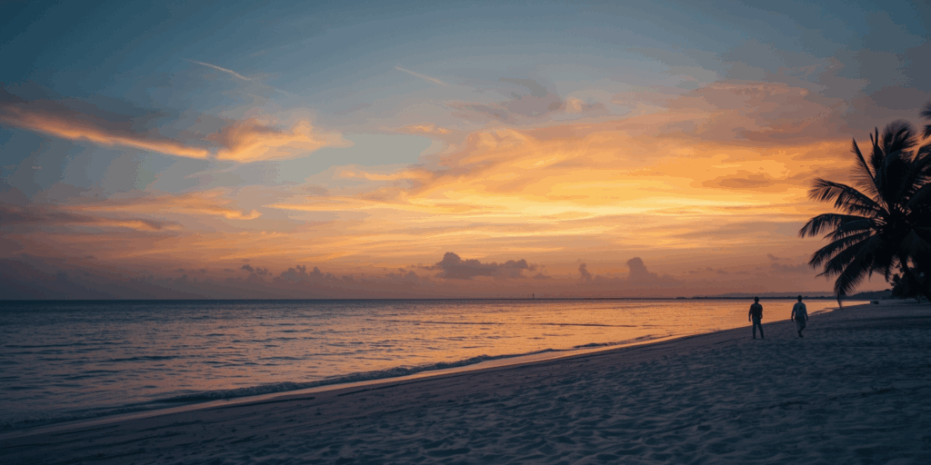 Pantai tersembunyi di Indonesia saat Beach Escape November, suasana senja tenang dengan dua orang berjalan di tepi air dan langit berwarna jingga lembut.