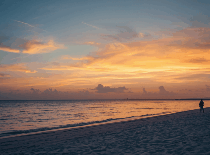 Pantai tersembunyi di Indonesia saat Beach Escape November, suasana senja tenang dengan dua orang berjalan di tepi air dan langit berwarna jingga lembut.